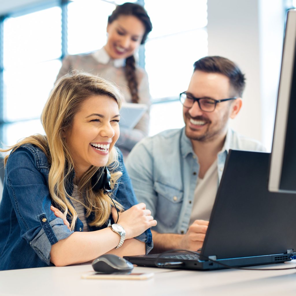 Drei glückliche Personen sitzen im Büro und schauen auf einen Bildschirm